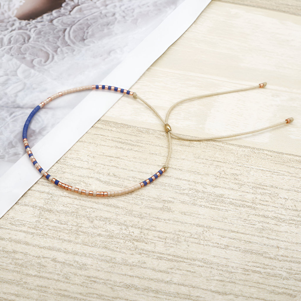 Bracelet fin en perles bleu, blanc et cuivre avec cordon réglable beige.