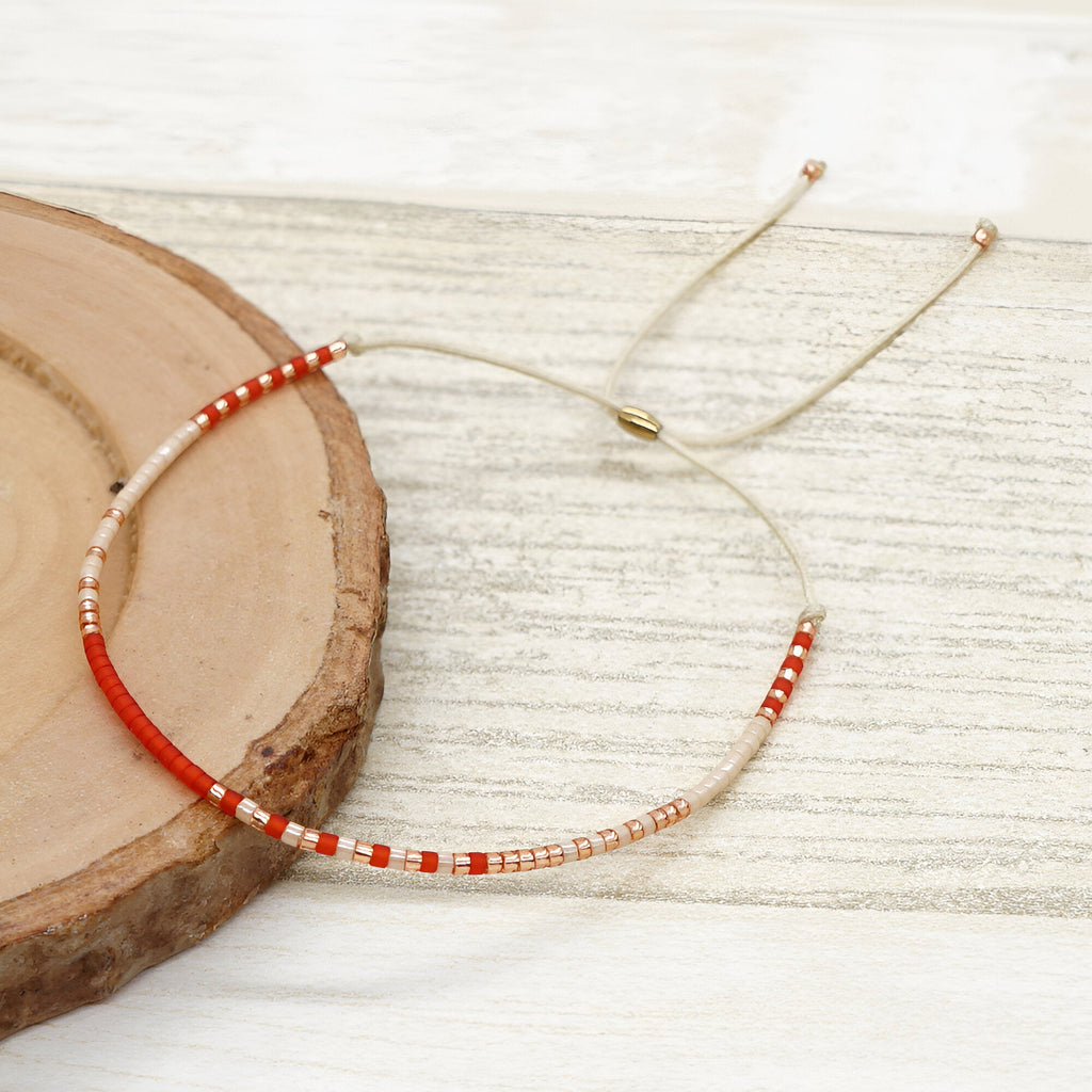 Bracelet fin en perles rouges et blanches, fil ajustable avec embouts dorés.