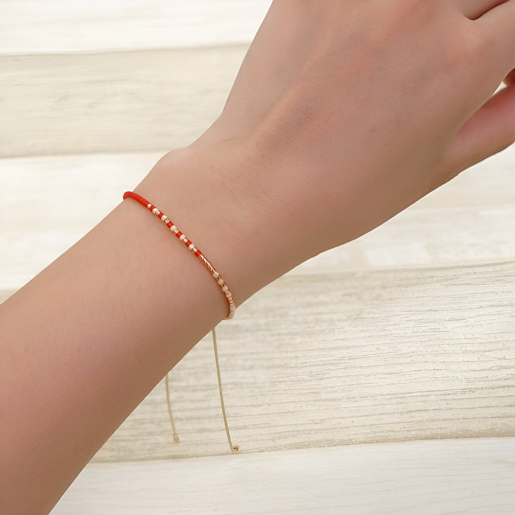 Bracelet fin en perles rouges et dorées avec chaîne réglable sur poignet féminin.