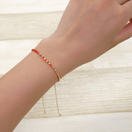 Bracelet fin en perles rouges et dorées avec chaîne réglable sur poignet féminin.