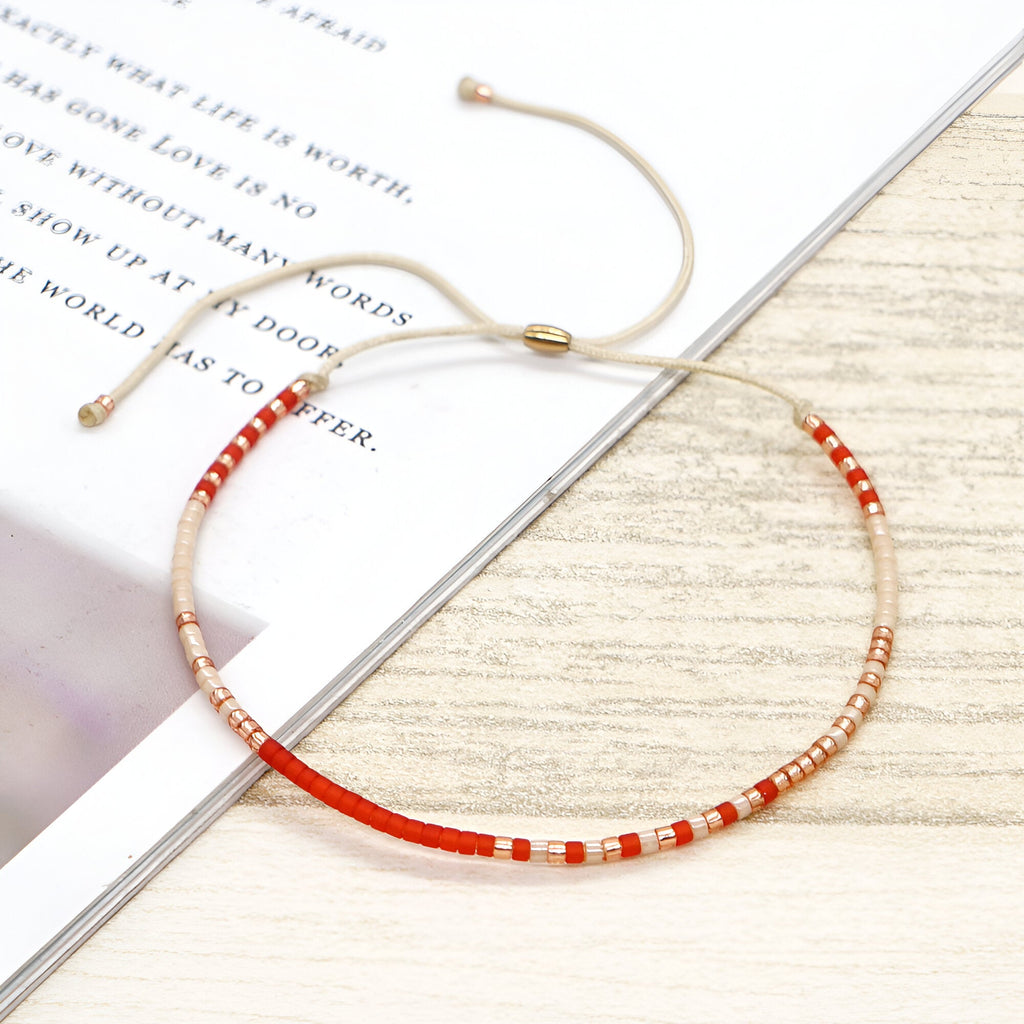 Bracelet fin réglable en perles rouges et dorées avec fil beige élégant.