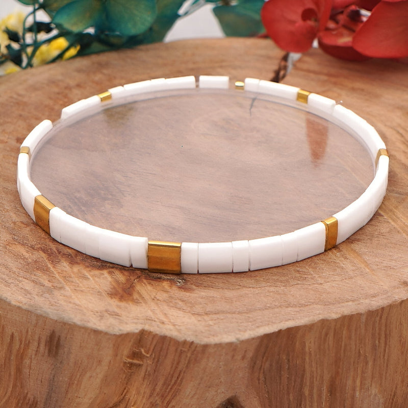 Bracelet fin en perles blanches cylindriques avec accents dorés, style minimaliste et élégant.