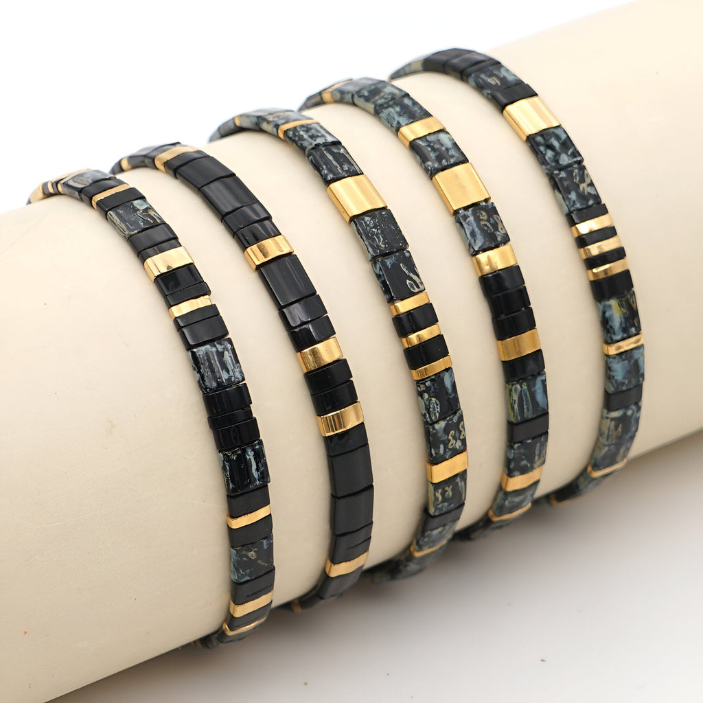 Bracelets en perles noires et dorées avec motifs variés sur support beige.