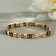 Bracelet marron en perles japonaises rectangulaires avec motifs dorés et blanc cassé.