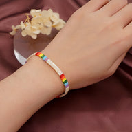 Bracelet multicolore en perles japonaises avec lettres blanches alignées sur poignet féminin.