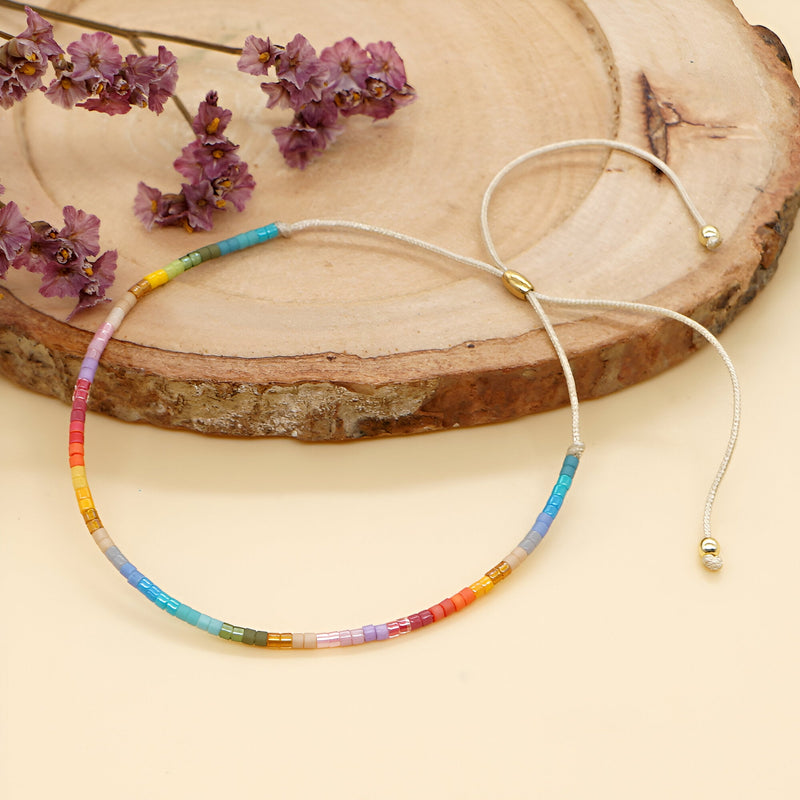 Bracelet fin en perles multicolores disposées en dégradé avec fermoir ajustable doré.