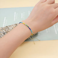 Bracelet fin en perles multicolores du Japon avec fermoir coulissant doré porté au poignet féminin.