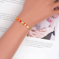 Bracelet fin femme en perles multicolores orange, jaune et rouge avec éléments dorés.