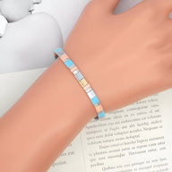 Bracelet femme en perles carrées bleu clair, blanc et beige avec élément doré élégant.