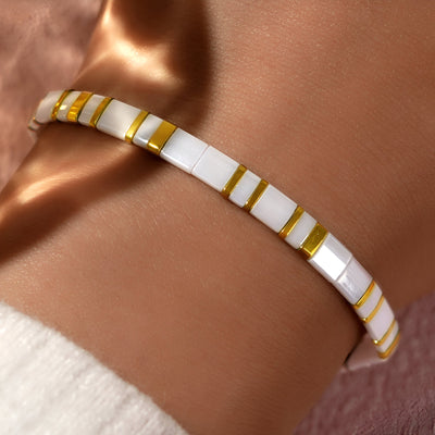 Bracelet femme en perles blanches carrées avec fines lignes dorées, style élégant et minimaliste.