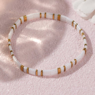 Bracelet féminin en perles blanches japonaises cylindriques avec anneaux dorés sur fond rose doux.