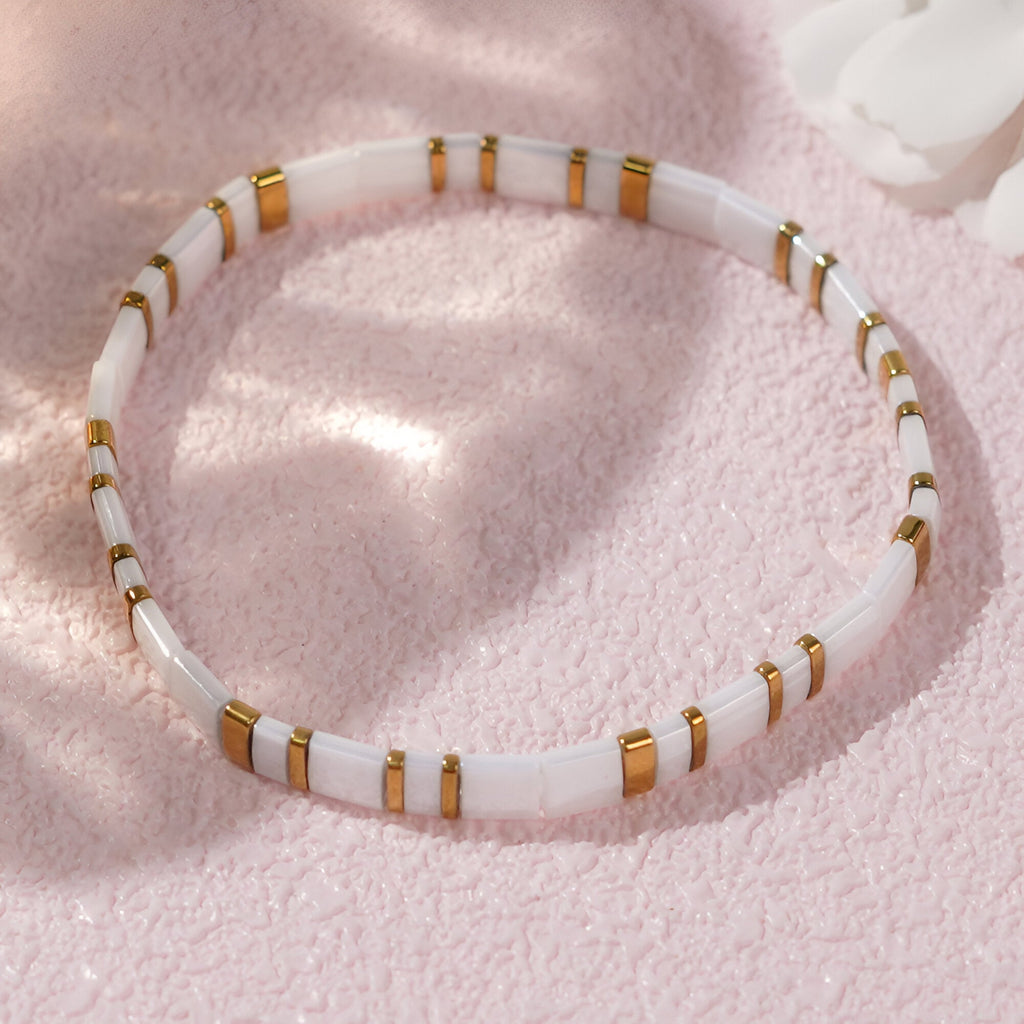 Bracelet féminin en perles blanches japonaises cylindriques avec anneaux dorés sur fond rose doux.