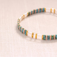 Bracelet fin en perles japonaises bleu turquoise, transparentes et blanches avec détails dorés.