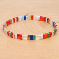 Bracelet fin en perles rectangulaires multicolores rouge, blanc, bleu, vert et transparent sur fond bois clair.
