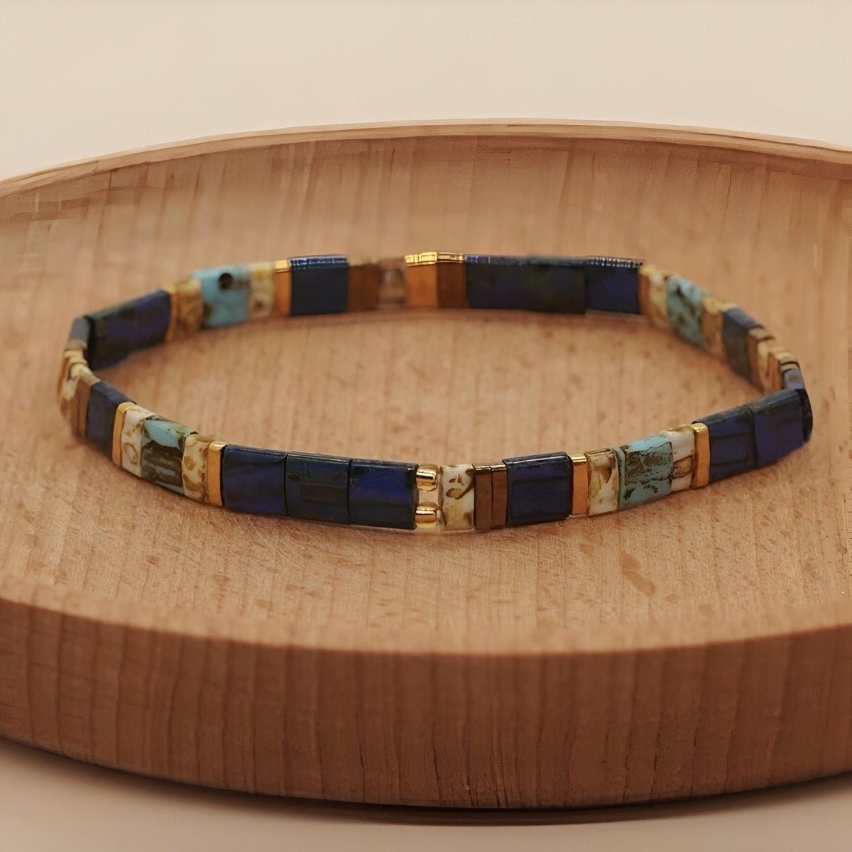 Bracelet femme perles carrées bleu marine et turquoise avec séparateurs dorés sur plateau en bois clair.