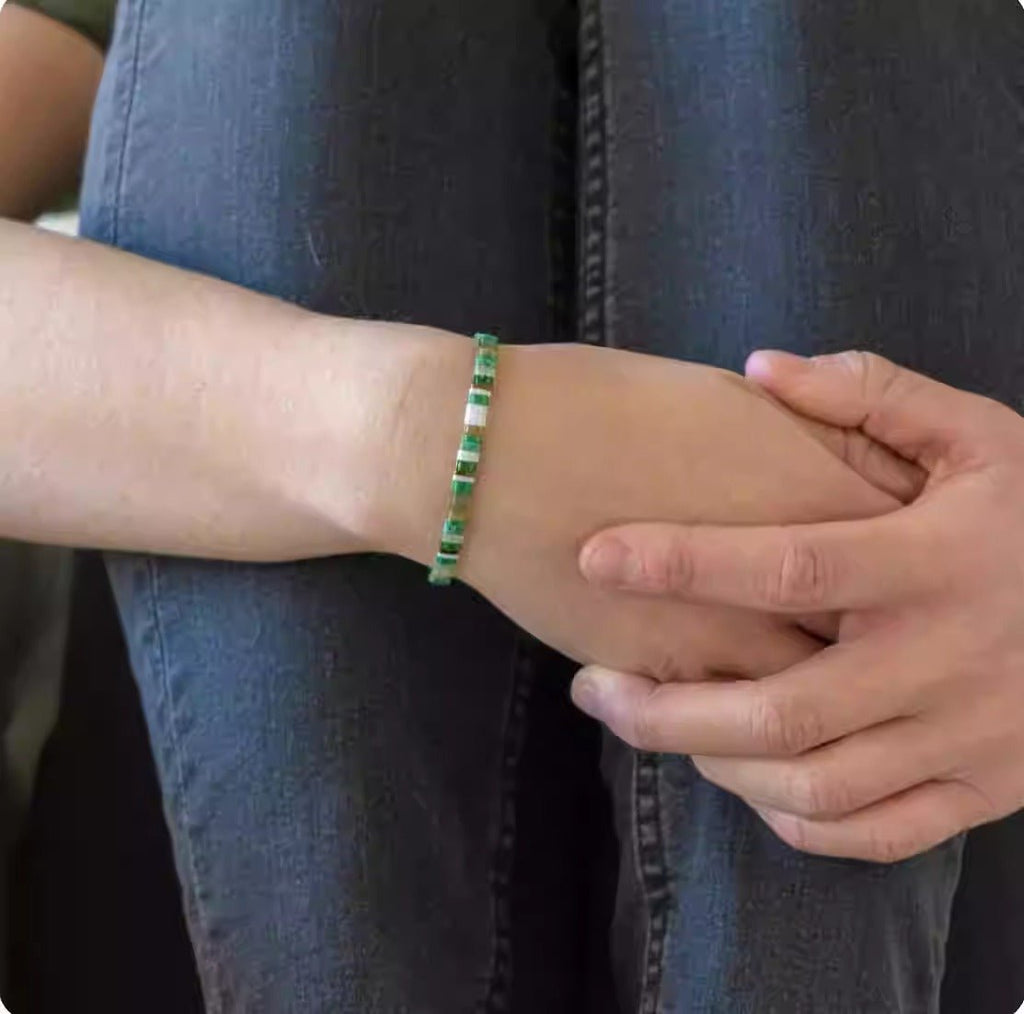 Bracelet vert en perles japonaises rondes porté sur poignet féminin avec jeans bleu.