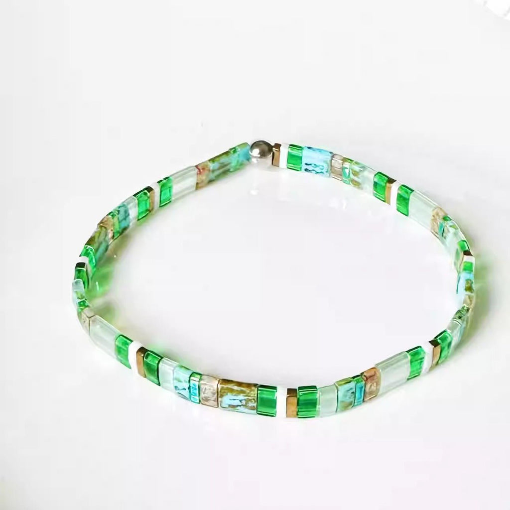 Bracelet fin en perles vertes et blanches avec fermoir métallique doré.