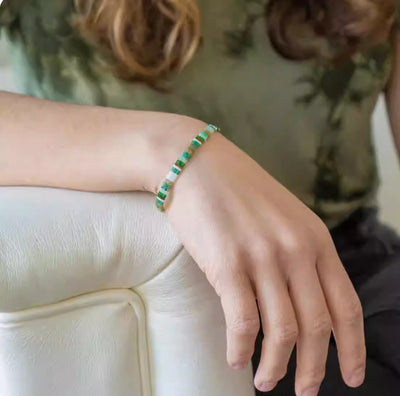 Bracelet fin avec perles vertes japonaises porté au poignet d'une femme sur fond flou.