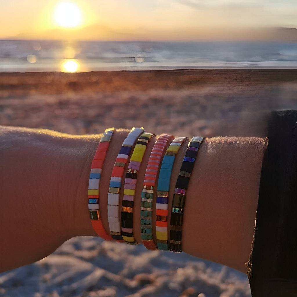 Bracelets en perles colorées du Japon, motif 1, portés au poignet, coucher de soleil en arrière-plan.