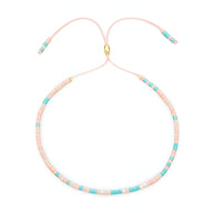 Bracelet fin en perles turquoise et rose clair avec fermoir doré et cordon ajustable rose pâle.