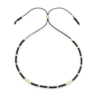 Bracelet Tsunada pour femme en perles noires et dorées sur cordon noir réglable.