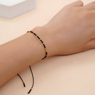 Bracelet fin en perles noires et dorées, style minimaliste, cordon ajustable.