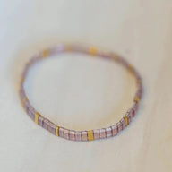 Bracelet fin en perles rose pâle avec intercalaires carrés dorés, style délicat et élégant.