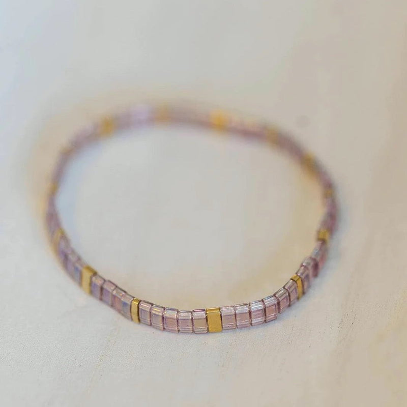 Bracelet fin en perles rose pâle avec intercalaires carrés dorés, style délicat et élégant.