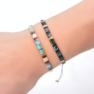 Deux bracelets fins en perles carrées, un en turquoise multicolore, l'autre noir et or sur un poignet clair.