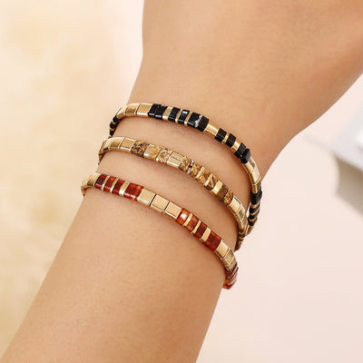 Bracelet souple à enfiler en perles japonaises multicolores rouges, noires et dorées avec accents brillants.