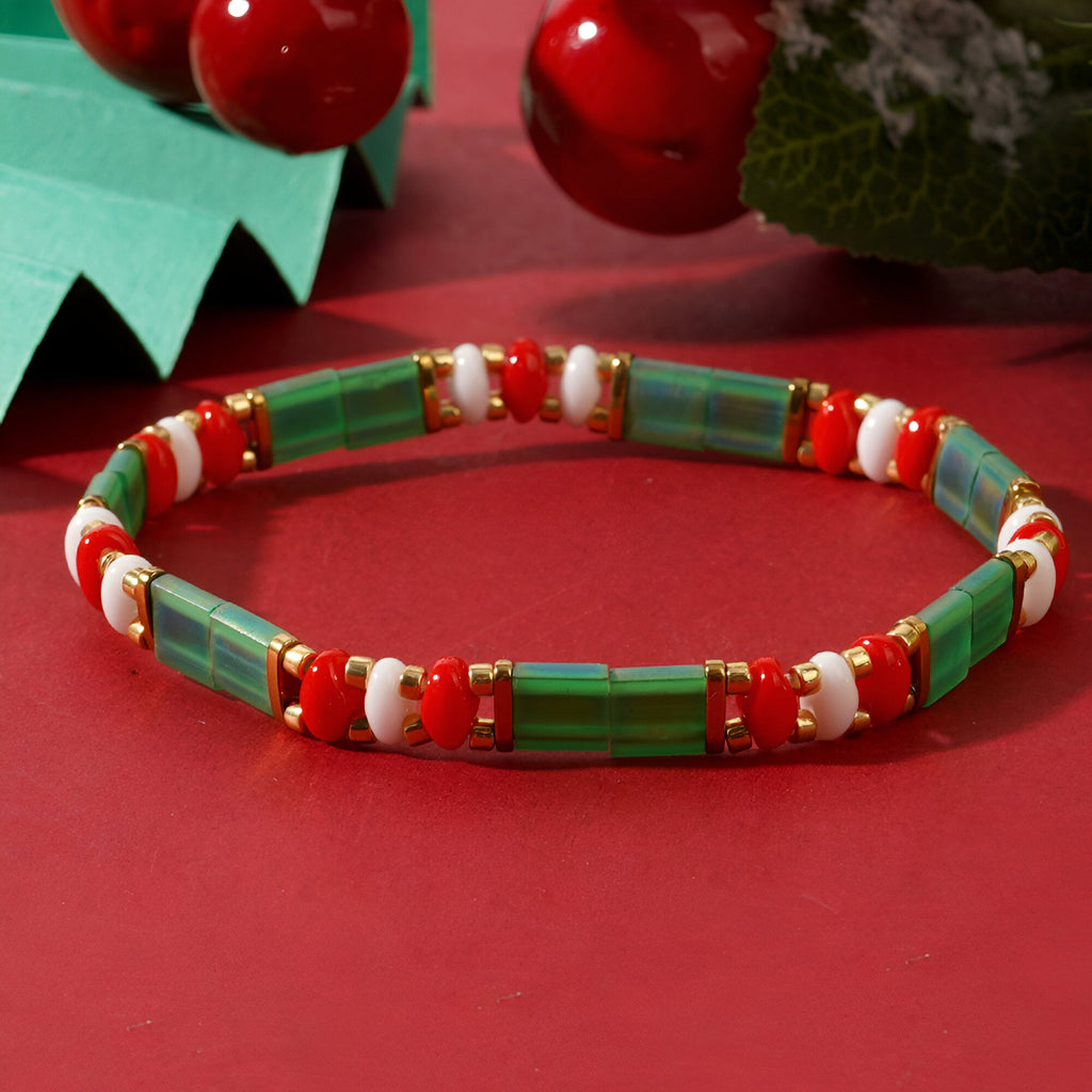 Bracelet féminin en perles vertes, blanches et rouges style Noël, modèle Santana sur fond rouge festif.