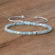 Bracelet ajustable perles heishi aigue-marine bleu clair avec intercalaires argentés sur cordon fin blanc.