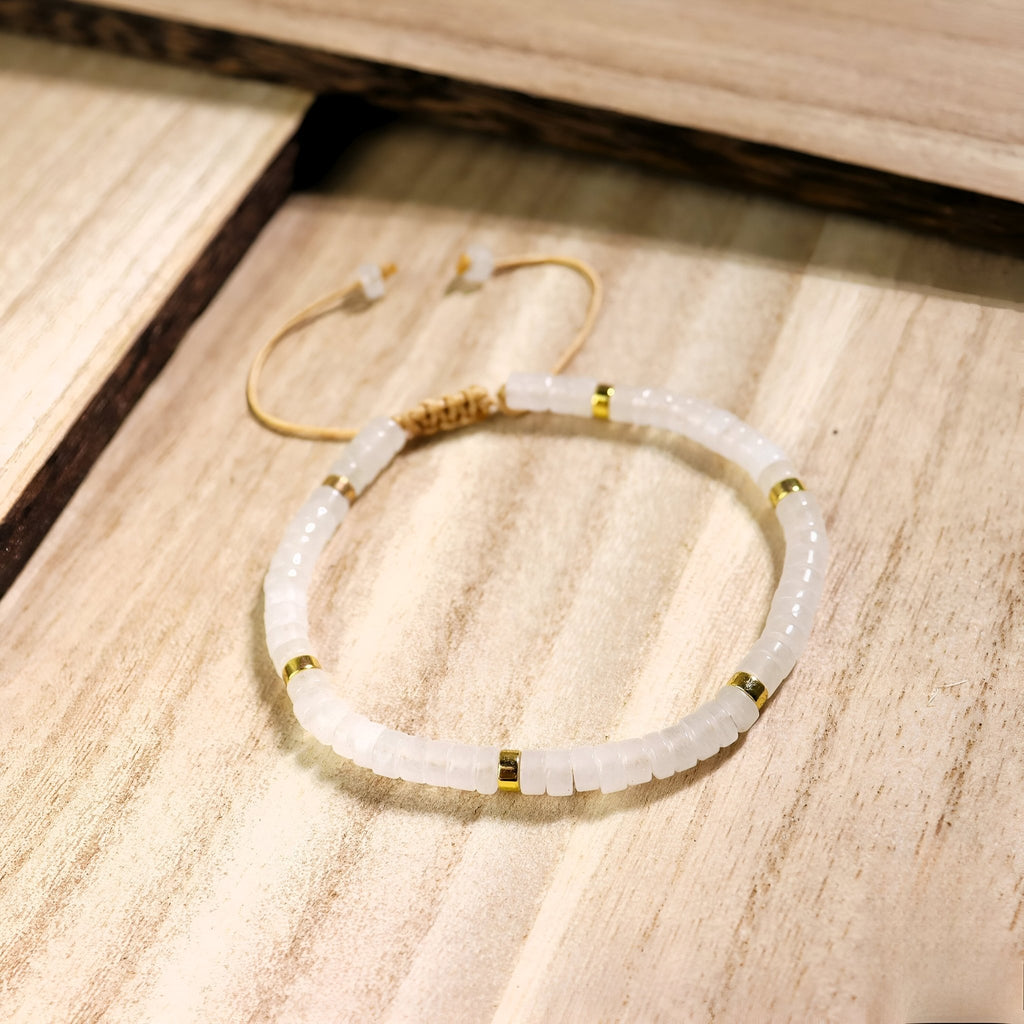 Bracelet mixte en perles heishi blanches et intercalaires dorés, modèle Riko, sur fond bois clair.