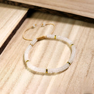 Bracelet mixte en perles heishi blanches et intercalaires dorés, modèle Riko, sur fond bois clair.