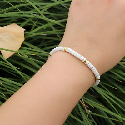Bracelet mixte en perles heishi blanches avec petites perles dorées sur poignet, style minimaliste.