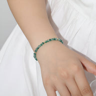 Bracelet fin en pierre d’agate verte aux reflets aquatiques, porté sur poignet féminin avec robe blanche.