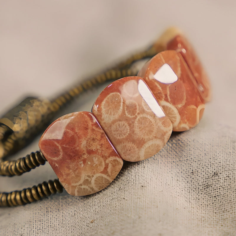 Bracelet femme en pierre de corail orange et cuivre avec perles carrées polies sur fond beige.