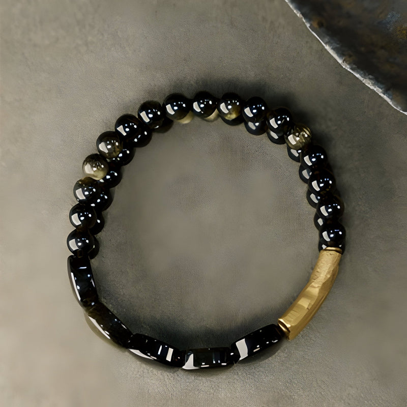 Bracelet femme en perles d’obsidienne noire et éléments en laiton doré, modèle Anica, taille ajustable.