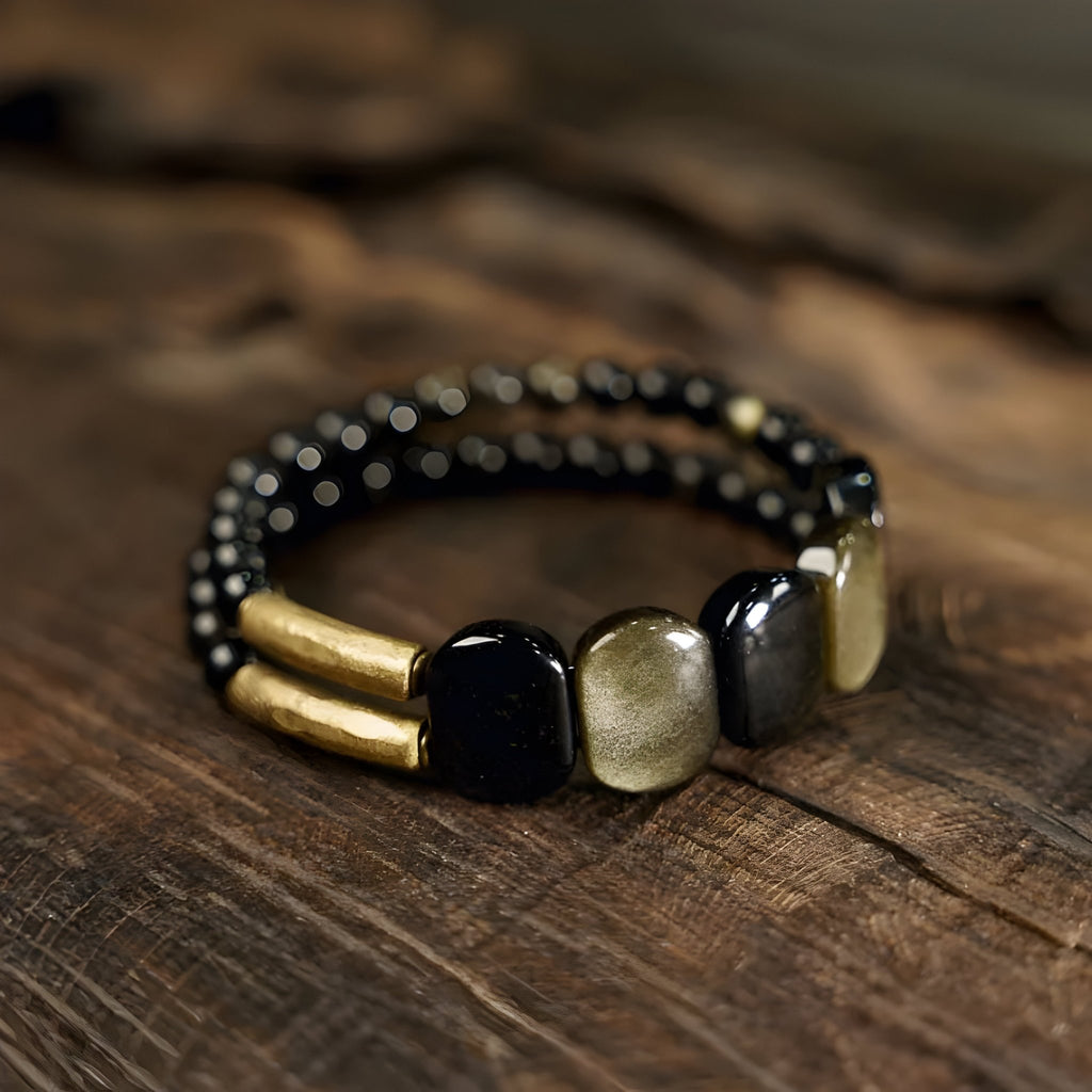 Bracelet femme en obsidienne dorée et laiton avec perles noires et carrées dorées sur fond bois.