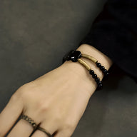 Bracelet femme en obsidienne dorée et laiton noir aux perles rondes et cœur central sur poignet.