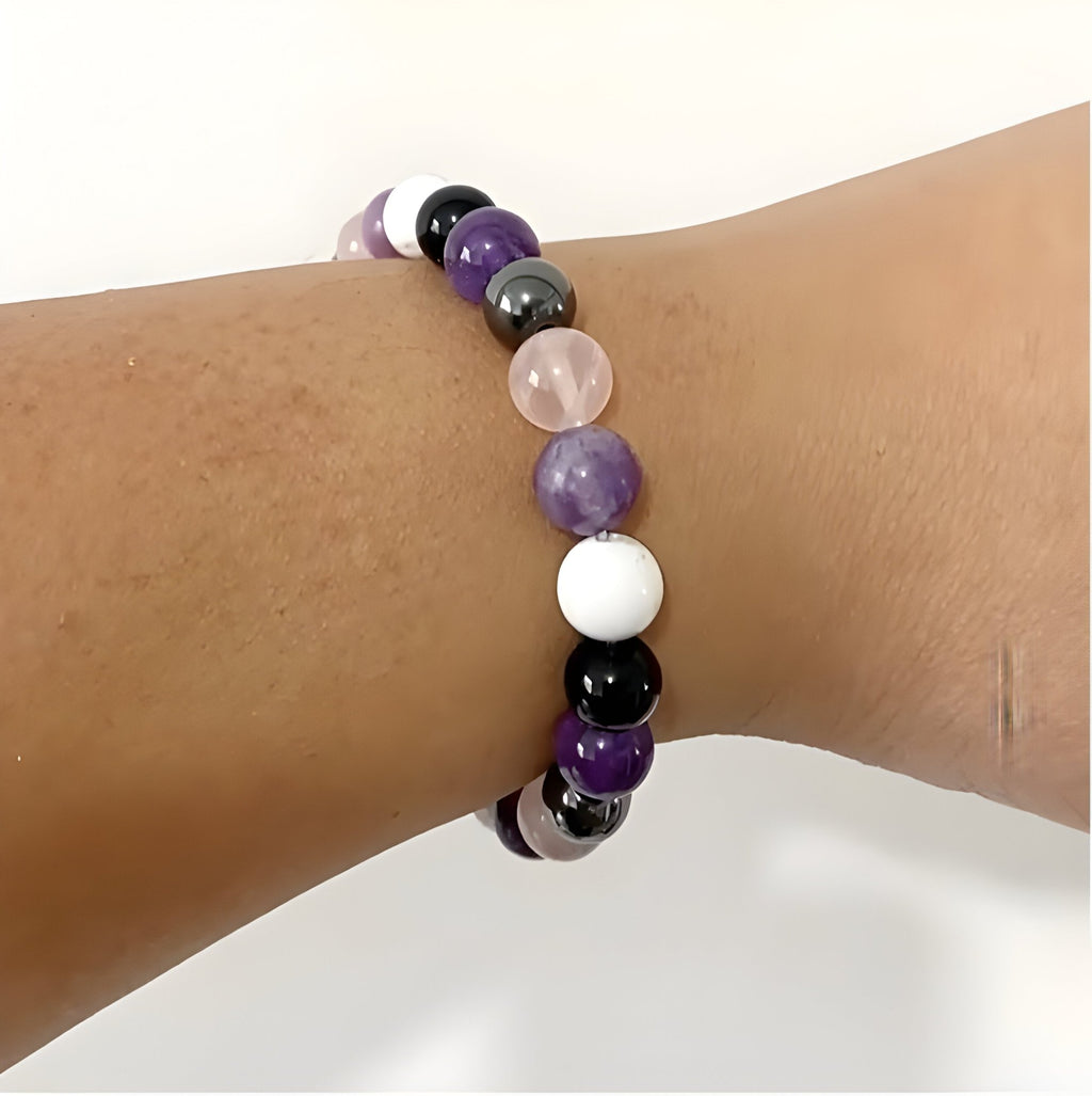 Bracelet perles naturelles violettes, blanches, noires et gris clair sur poignet.