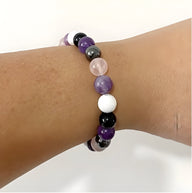 Bracelet perles naturelles violettes, blanches, noires et gris clair sur poignet.