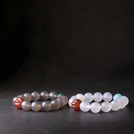 Deux bracelets en perles d'agate, l'un gris avec une perle rouge, l'autre blanc mat avec une perle rouge, design mixte.