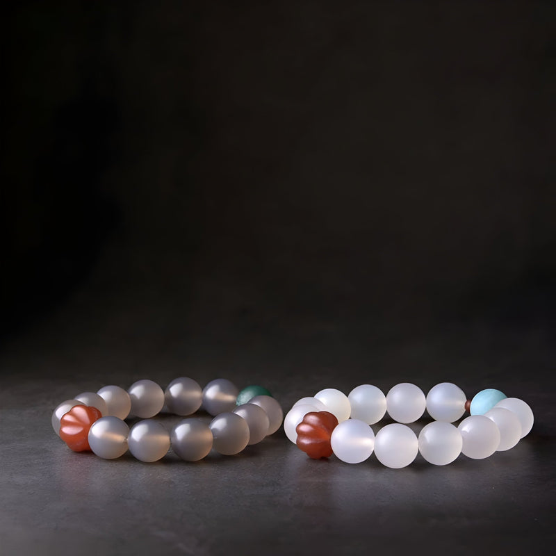 Deux bracelets en perles d'agate, l'un gris avec une perle rouge, l'autre blanc mat avec une perle rouge, design mixte.
