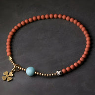Bracelet femme en perles d'agate rouge mate avec perles dorées, perle turquoise et pendentif trèfle doré.