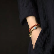 Bracelet femme en agate rouge avec perles dorées et pendentif trèfle sur poignet.