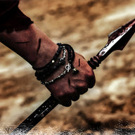 Bracelet homme pierres naturelles noires avec pendentif ornement spartiate en métal gris sur poignet brun foncé.