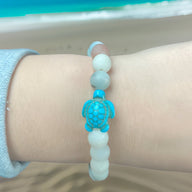 Bracelet mixte en pierre blanche avec une tortue turquoise sculptée au centre.