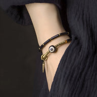 Bracelet femme en pierres noires d'agate et cuivre doré avec pendentif œil protecteur, style minimaliste.