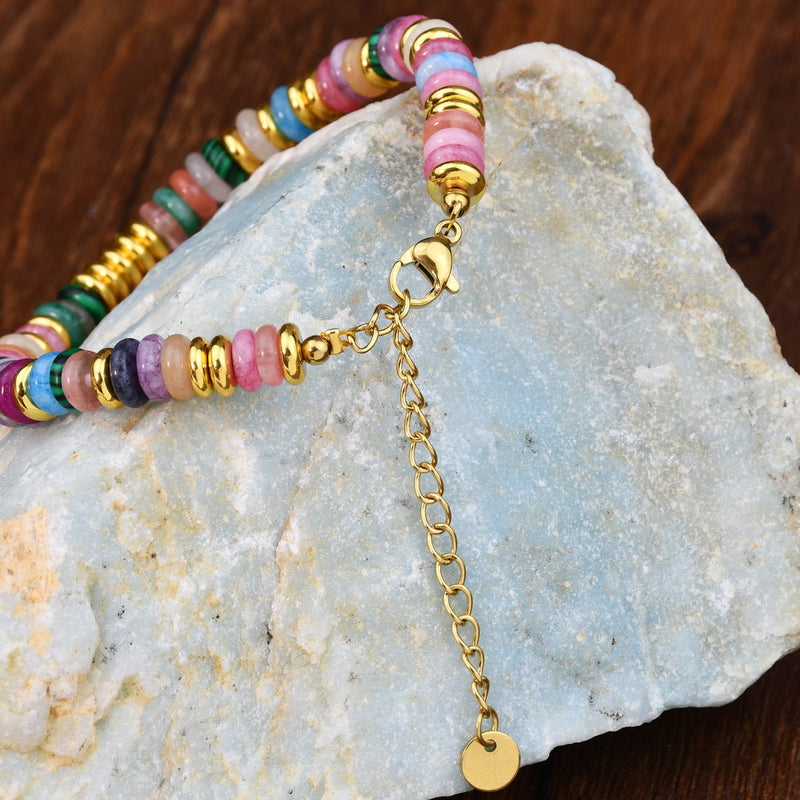 Bracelet femme en pierres de cristal multicolores avec fermoir doré et chaîne réglable sur pierre grise.